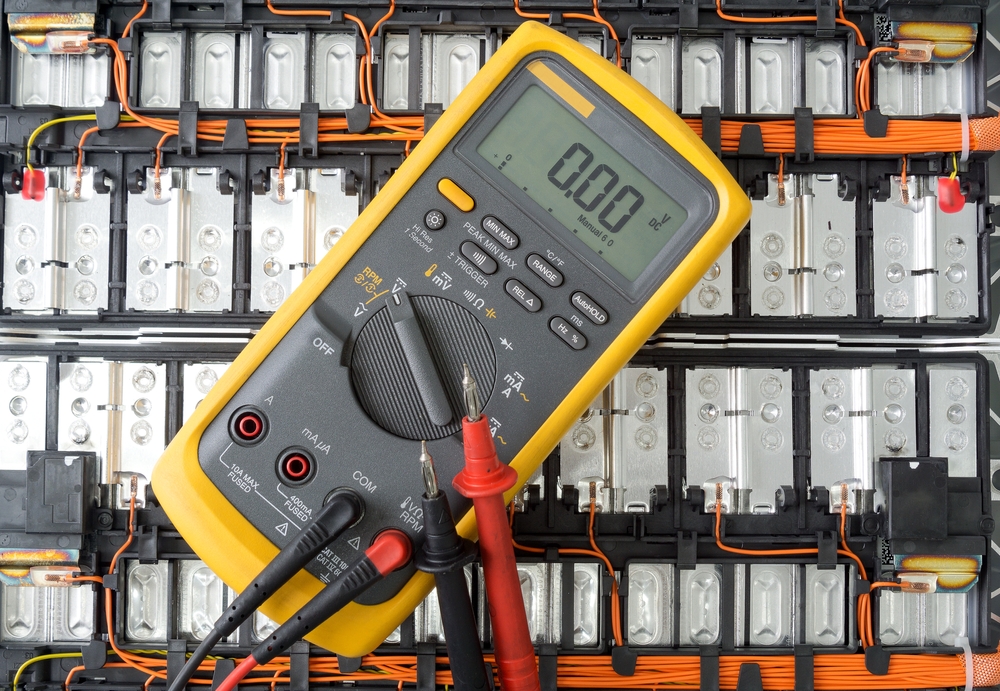 Yellow,Digital,Multimeter,With,Probes,On,Lithium,Ion,Battery,Background